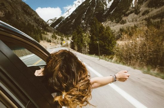 woman riding on vehicle putting her head and right arm outside the window while travelling the road