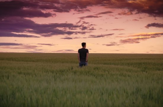 man standing between tall grasses during golden hour